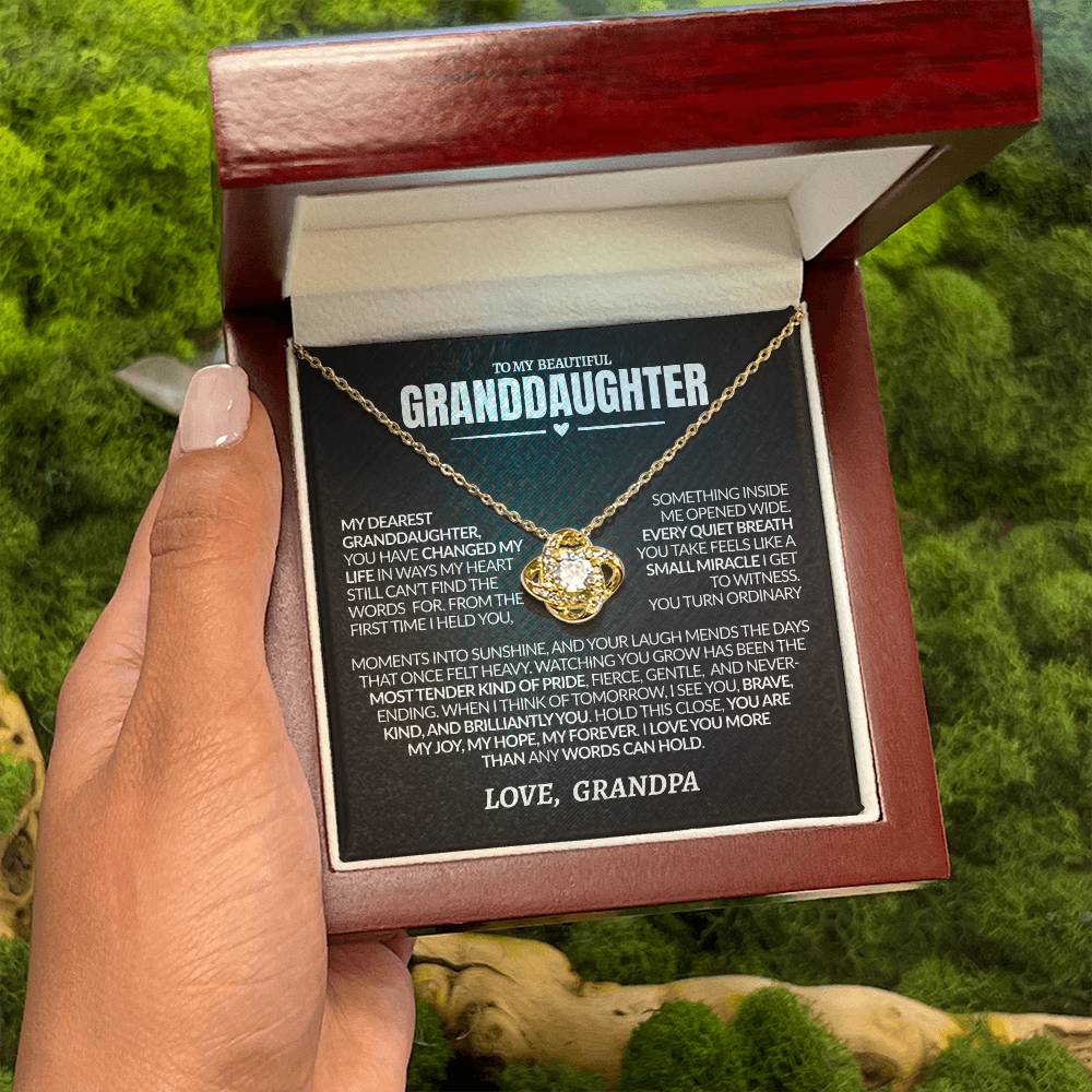 Gold necklace with heart-shaped pendant in a wooden box, held by a hand against a green natural background.