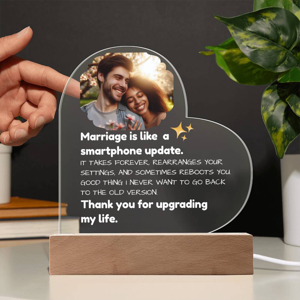 Heart-shaped plaque with a humorous quote about marriage, held by a hand with a plant in the background.