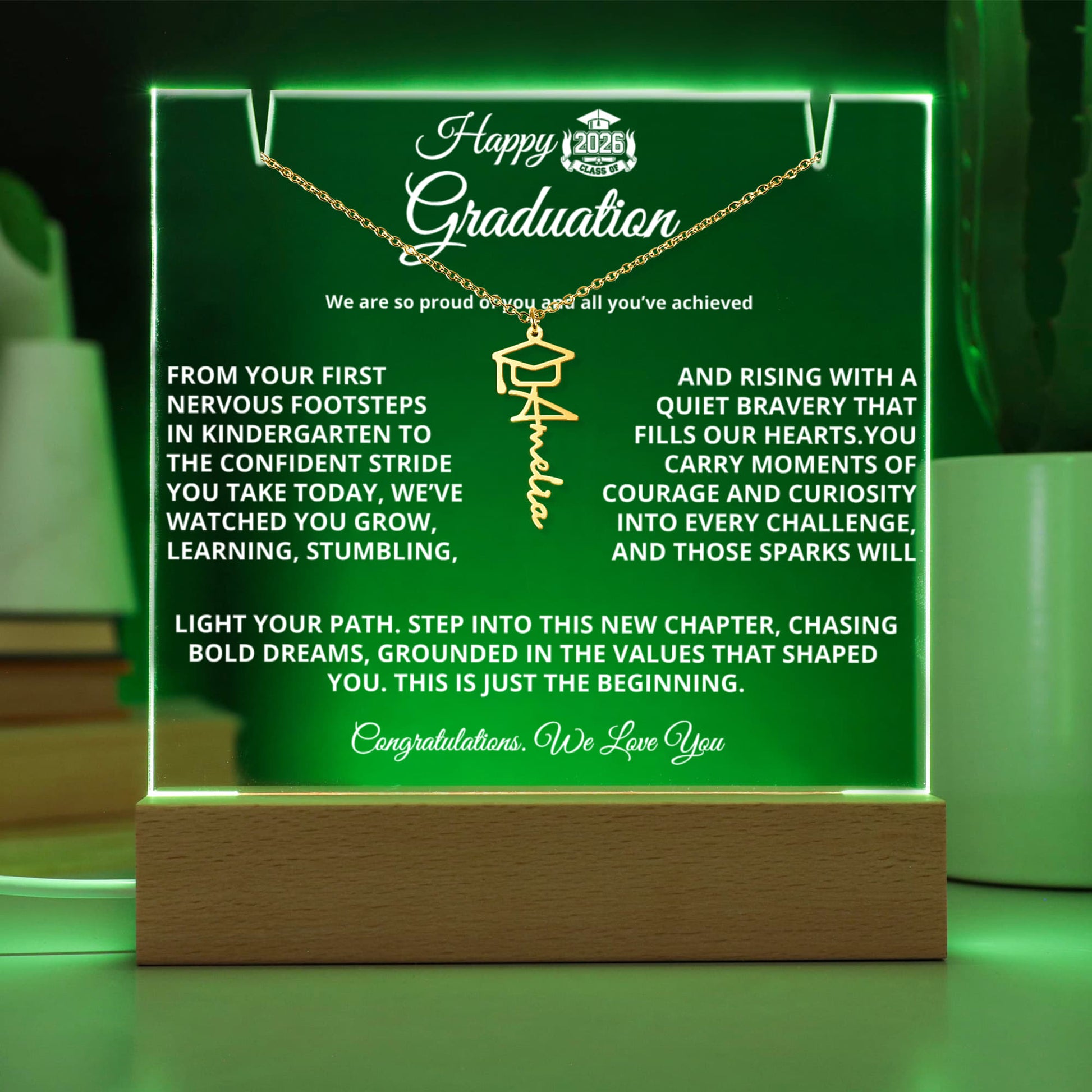 Graduate’s desk with a glowing personalized acrylic plaque on a wooden LED base and a Graduation Cap Name Necklace — perfect dorm or display piece.